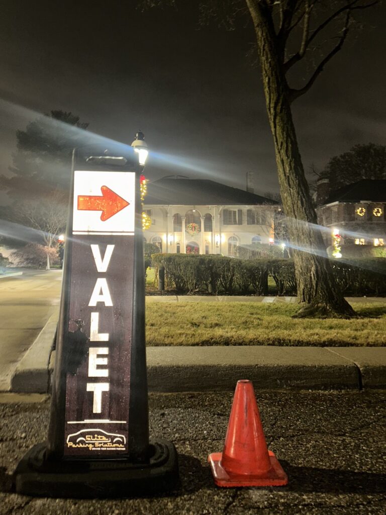 A professional valet parking stand and traffic cone positioned curbside at night to guide arriving guests.