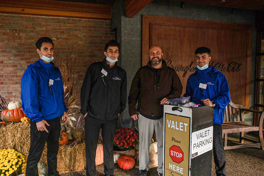 Discover why choose us for reliable vehicle management, featuring our professional attendants standing next to a valet parking stand.